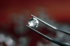 Pinzas sosteniendo un diamante sobre fondo rojo.