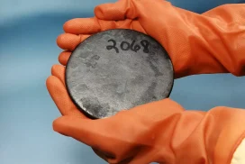 Manos con guantes sostienen disco metálico numerado.